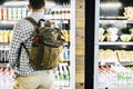 Rear view of man in backpack standing against cold drink beverage store. Man choosing drink in supermarket. Back of male customer Royalty Free Stock Photo