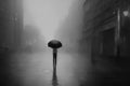 Rear view of man in black coat with umbrella walking in rain on city street in evening.