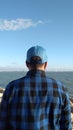 Rear view of a man in a blue checked shirt and cap enjoying a view of an ocean Royalty Free Stock Photo