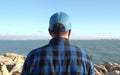 Rear view of a man in a blue checked shirt and cap enjoying a view of an ocean Royalty Free Stock Photo