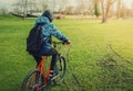 Rear view of a man cyclist riding a bike early spring morning in the park. Tourist with a backpack and hoodie on a bicycle