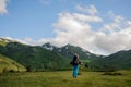 Rear view man on the hill looking at rocky mountains covered with grass with the snow remnants Royalty Free Stock Photo