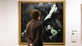 Rear view of man looking at painting in Museum. Concept. Young man looks at dark painting with demons in Museum of