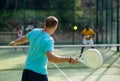 Rear view of man playing paddle tennis match on outdoor court on blurred background of opponents. Sport lifestyle