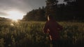 Rear view of a man running through wild green field with long grass. Stock footage. Camera follows runner in beautiful