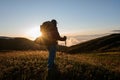 Rear view man standing on the hill field with hiking backpack and sticks looking at the sun Royalty Free Stock Photo