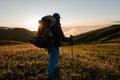 Rear view man standing on the hill field with hiking backpack and sticks looking at the sunrise Royalty Free Stock Photo