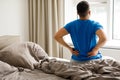 Rear view of a man touching and massaging his spine suffering from pain after sleeping on an uncomfortable bed. Royalty Free Stock Photo