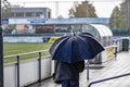 Rear view of a man walking with an umbrella on rainy day next to a soccer field Royalty Free Stock Photo