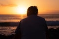 Rear view of mature man at sea looking at the horizon and at the orange sunset light Royalty Free Stock Photo
