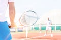 Midsection of mature man holding racket while playing with friends on tennis court