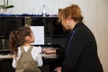 Rear view mature woman, pianist teacher giving music lesson to a smart child girl, teaching her playing on grand piano