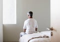 Rear view of middle aged man sitting on edge of bed in bedroom Royalty Free Stock Photo