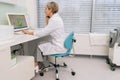 Rear view of middle-aged woman general practitioner sit at desk in clinic office looking at laptop screen, discuss Royalty Free Stock Photo