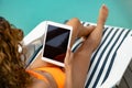 Woman using digital tablet while relaxing on a sun lounger near swimming pool at the backyard of hom Royalty Free Stock Photo