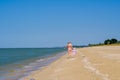 Rear view of a mother and a baby girl walking along a deserted sandy sea beach along the surf against a blue cloudless Royalty Free Stock Photo