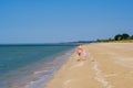 Rear view of a mother and a baby girl walking along a deserted sandy sea beach along the surf against a blue cloudless Royalty Free Stock Photo