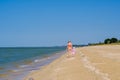 Rear view of a mother and a baby girl walking along a deserted sandy sea beach along the surf against a blue cloudless Royalty Free Stock Photo