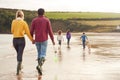 Rear View Of Multi-Cultural Family With Pet Dog Walking Along Beach Shoreline On Winter Vacation Royalty Free Stock Photo