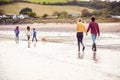 Rear View Of Multi-Cultural Family With Pet Dog Walking Along Beach Shoreline On Winter Vacation Royalty Free Stock Photo