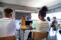 Rear view of multiracial group of teen high school students in classroom listen to male teacher explaining lesson. Royalty Free Stock Photo