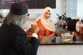 Rear view muslim customer businessman wearing black suit drinking coffee at counter with young muslim barista girls background