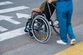 Rear view of a nurse helping an elderly woman in a wheelchair cross the road.