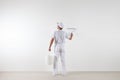 Rear view of painter man looking at blank wall, with paint roller and bucket, isolated on white room Royalty Free Stock Photo