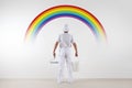 Rear view of painter man looking rainbow at blank wall, with paint roller and bucket, isolated on white