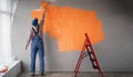 Rear view of painter man painting the wall in orange color with paint roller, empty space with red ladder Royalty Free Stock Photo