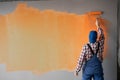 Rear view of painter man painting the wall with paint roller and orange color. Big empty space Royalty Free Stock Photo