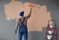 Rear view of painter man painting the wall with paint roller in orange colour, isolated on empty space with red ladder Royalty Free Stock Photo