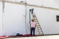 Rear view of painter man painting the wall, with paint roller, in a white village of Huelva, Spain