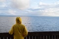 Man tourist in yellow raincoat watching sea on cold cloudy day looking at water, listening waves Royalty Free Stock Photo