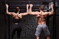 Rear view photo of couple of man and woman in the sportwear making exercise on a horizontal bar against brick wall. Royalty Free Stock Photo