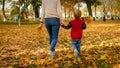 Rear view photo of little boy holding his mother by hand and walking at autumn park Royalty Free Stock Photo