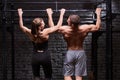 Rear view photo of the muscular man and woman doing exercises on horizontal bar against brick wall at the cross fit gym. Royalty Free Stock Photo