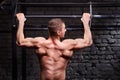 Rear view photo of the young muscular male doing exercises on horizontal bar against brick wall at the cross fit gym.
