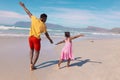 Rear view of playful african american young man and daughter with arms outstretched running at beach Royalty Free Stock Photo