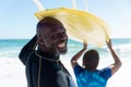 Rear view portrait of african american senior man carrying surfboard on head with woman at beach Royalty Free Stock Photo