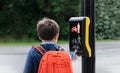 Rear view portrait School kid pressing a button at traffic lights on pedestrian crossing on way to school. Child boy with backpack Royalty Free Stock Photo