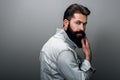 Rear view portrait of stylish brutal young Caucasian male with thick beard wearing trendy denim jacket, staring at camera with