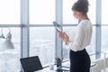 Rear view portrait of a young female office worker using apps at her tablet computer, wearing formal suit, standing near Royalty Free Stock Photo