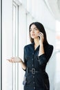 Portrait of young worker speaking using cell phone, looking out the window. Female having business call, busy at her workplace. Royalty Free Stock Photo