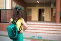 Rear view of a pretty little girl returning from school with a backpack in a yard