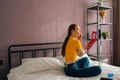 Rear view of pretty young redhead woman using blusher with makeup brush in front of mirror sitting on bed. Back view of Royalty Free Stock Photo