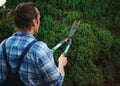 Rear view male gardener in blue gardening work uniform, trimming, pruning and shaping boxwood, buxus using hedge shears Royalty Free Stock Photo