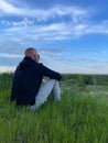 Rear view of relaxed young man sitting on grass against blue sky. Royalty Free Stock Photo