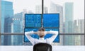 Rear view of a relaxing trader who is sitting in front of a trading station which consists of four screens with financial data. A