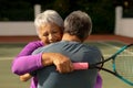 Rear view of romantic biracial senior man embracing smiling wife holding racket at tennis court Royalty Free Stock Photo